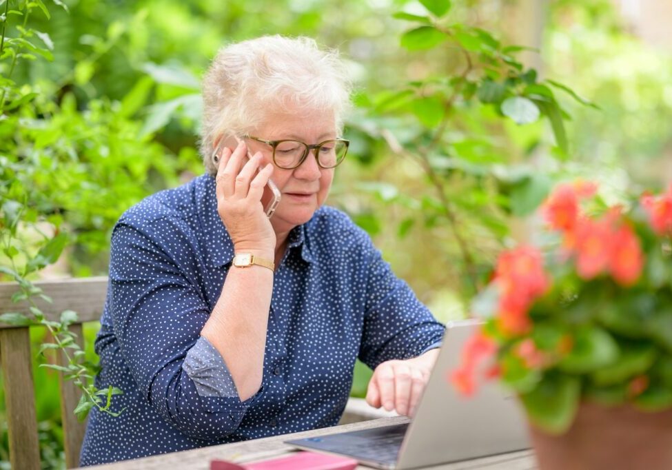 Woman on the phone while using a laptop in her garden