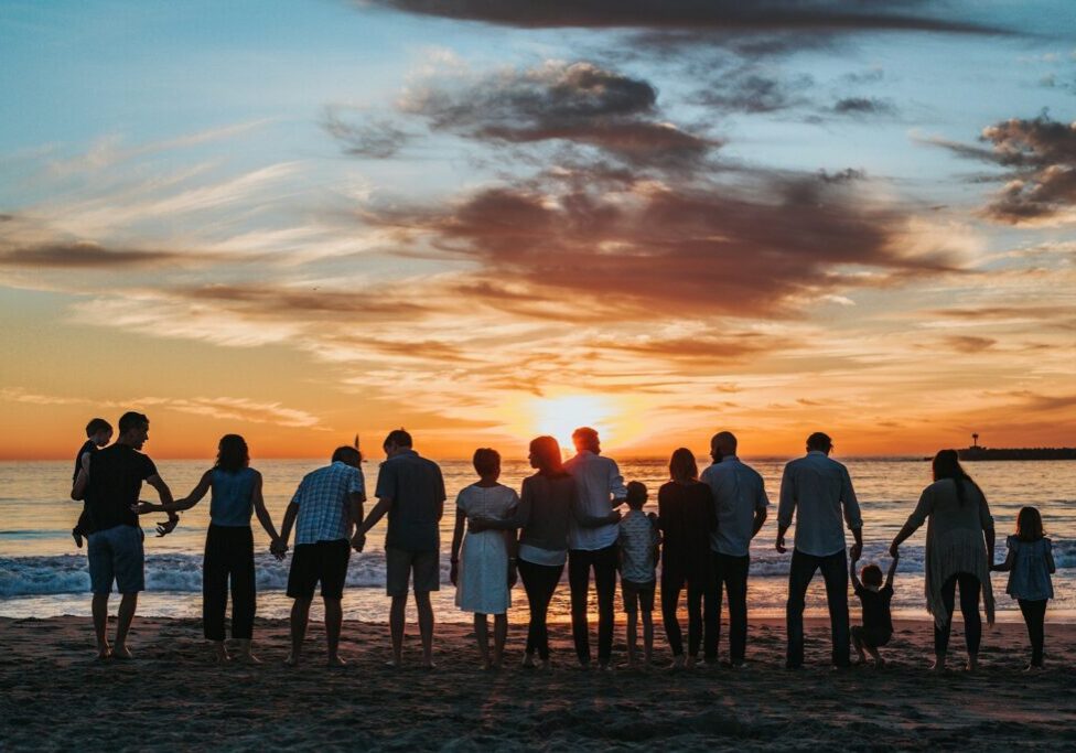 Extended family holding hands on a beach at sunset